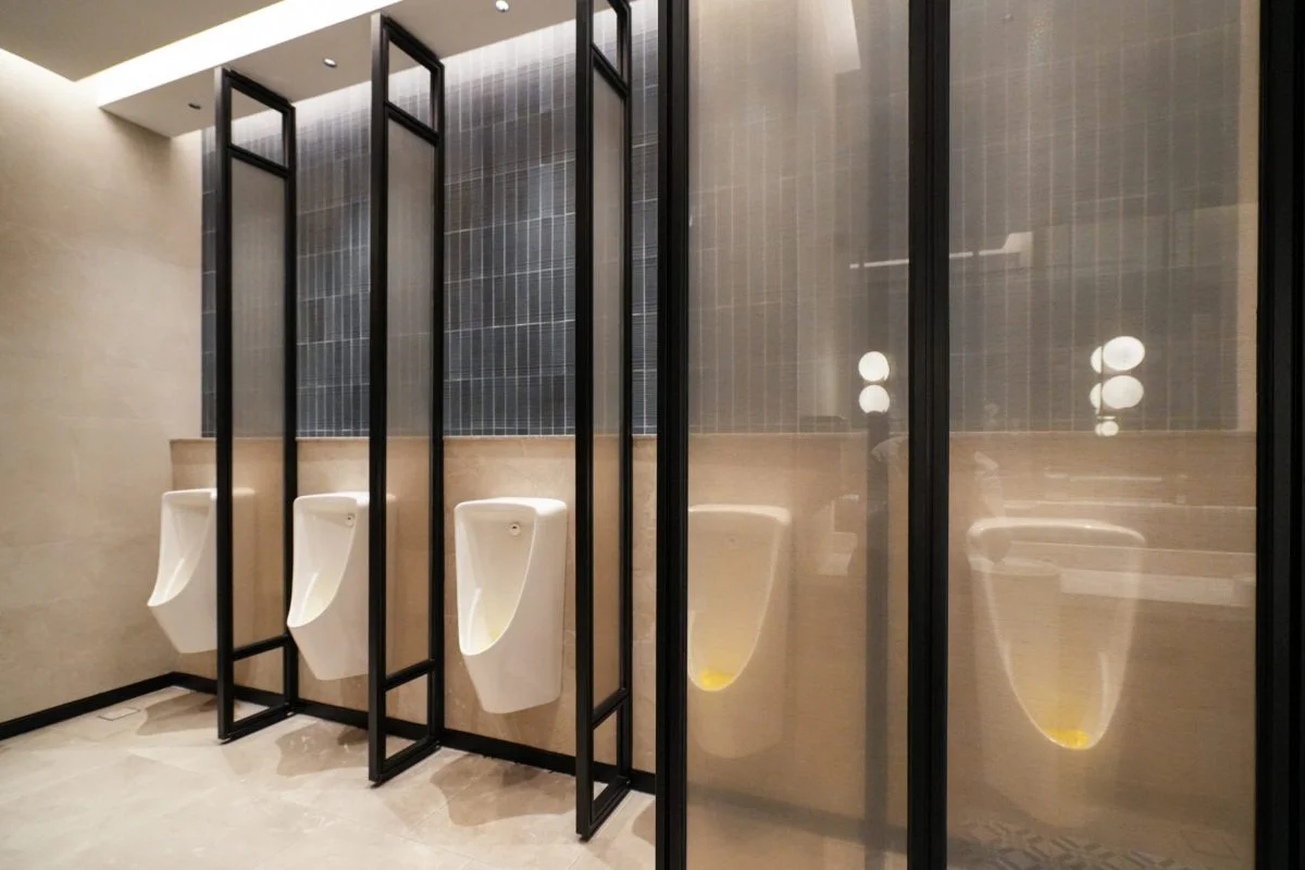 Wall-mounted urinals with black metal and glass partitions in the Gents washroom.