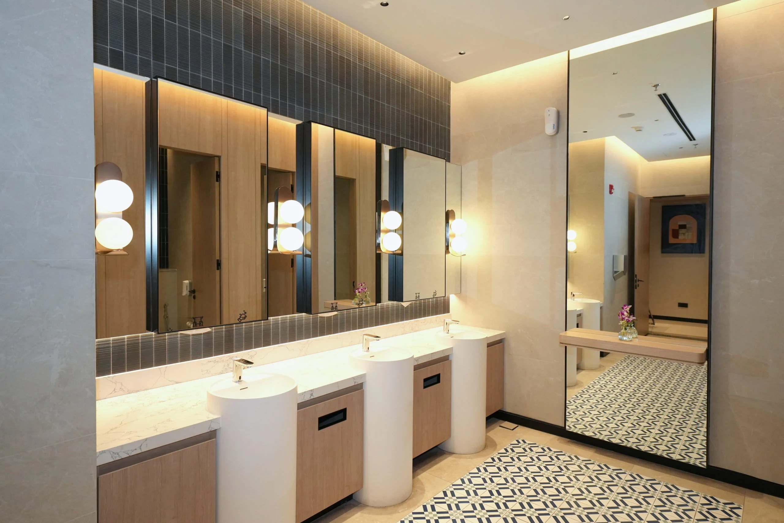 Cylindrical basins, a marble countertop and backlit mirrors in the Ladies washroom.